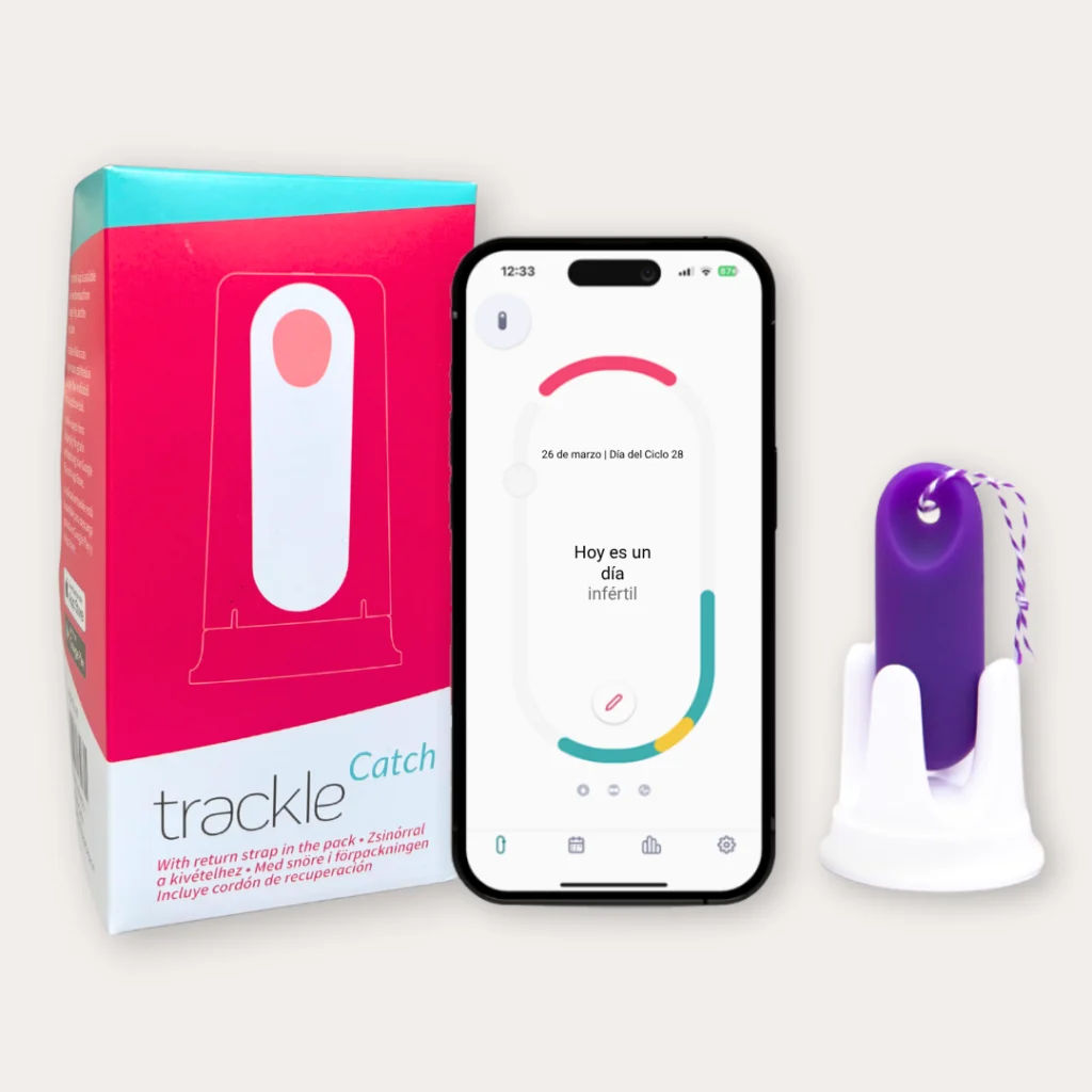 Fotografía del producto trackle Catch que muestra su caja rosa y blanca, un smartphone con la aplicación abierta indicando 'Hoy es un día infértil' y el sensor de temperatura morado con cordón de retorno en su base.