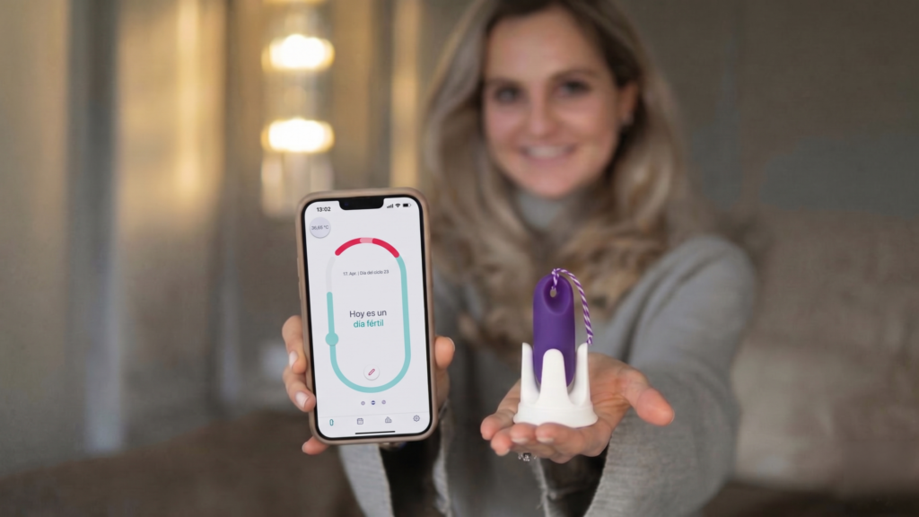 Una mujer sonriente sostiene el sistema de sensores Trackle en un soporte y muestra ante la cámara un smartphone con la aplicación de ciclo abierto.